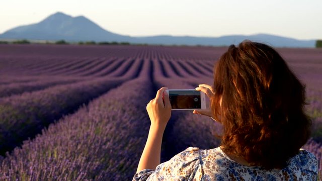 Woman taking a pictures of endless lavender field with her smartphone