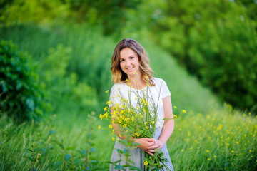 girl walks in the park, holds a bouquet of wild flowers in hand and smiles