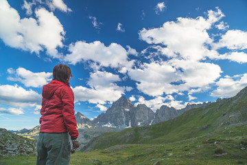 Naklejka premium One person looking at the majestic view of glowing mountain peaks at sunset high up on the Alps. Rear view, toned and filtered image, focus in the background.