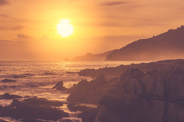 Obraz premium Wave splash on rock in sunset beach background. Copy space of outdoor summer vacation and business travel adventure concept.