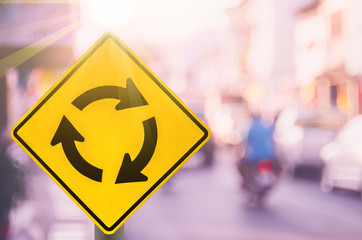 Roundabout warning sign on blur traffic road with colorful bokeh light abstract background.