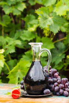 Black old balsamic vinegar in a glass jug with fresh red grapes on green vineyard background
