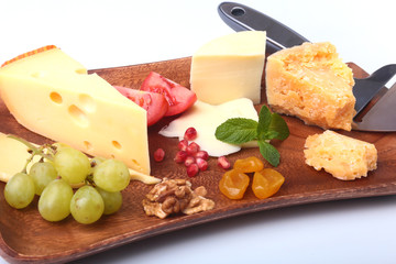 Assortment of cheese with fruits, grapes, nuts and cheese knife on a wooden serving tray.