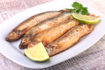 Deep frying small fish capelin and sliced lemon on white plate. Good snack to beer.