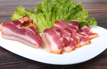 Fresh homemade smoked bacon with leaves lettuce on white plate. Selective focus.