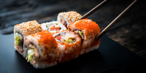 closeup of sushi rolls with chopsticks on dark background © Ievgen Skrypko
