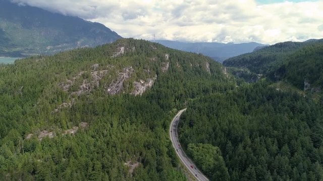 Helicopter View of Cars Traveling Scenic Highway into Thick Green Forest Mountains