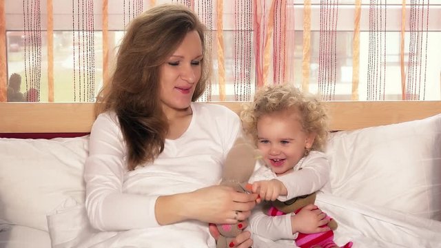 happy smiling mother with her child girl playing with toy cats on bed