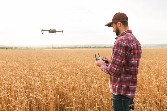 Farmer holds remote controller with his hands while copter is flying on background. Drone hovers behind the agronomist in wheat field. Agricultural new technologies and innovations. Back view