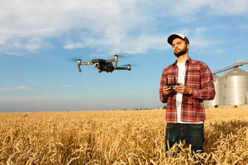 Drone hovers in front of farmer with remote controller in hands near grain elevator. Quadcopter...