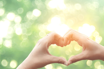 Female hands heart shape on nature green bokeh sun light flare and blur leaf abstract background.