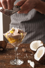 Culinary art of fresh fruit salad in martini glass with coconut flakes. Unrecognizable man makes a sweet dessert with decoration