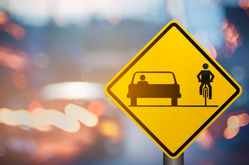 Bicycle and car share warning sign on blur traffic road with colorful bokeh light abstract background.