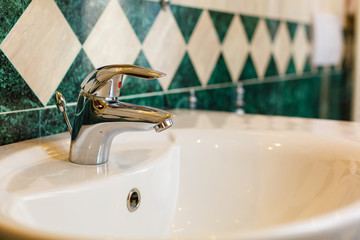Chrome mixer on white ceramic Washbasin in a retro style white green bathroom.