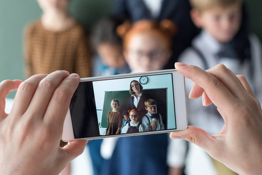 close-up view of young female teacher and cute little students photographing with smartphone