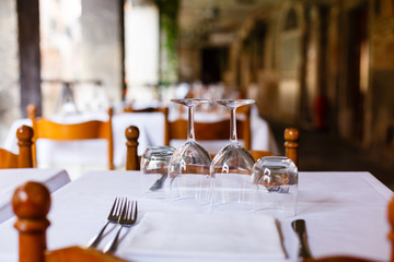 Empty inverted glasses on a wooden table with white tablecloth in a restaurant