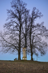 Three trees and calvary chapel with a bench in nature, vertical natural photo