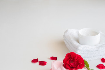 Obraz na płótnie Canvas Body cream jar on the white, soft towels with fresh, red rose for fragrant atmosphere on the white background.