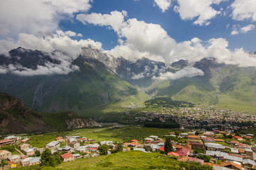 Fototapeta na wymiar Stepantsminda and Gergeti villages in Kazbegi region with Rocky Caucasus mountains and cloudy sky background