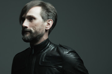 Obraz premium Portrait of fashionable handsome mature hipster in black leather jacket over sark grey background. Close up. Copy-space. Studio shot