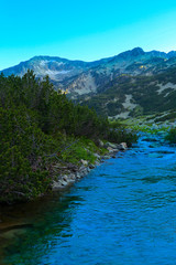 Fototapeta na wymiar Beautiful view on the high green mountains peaks and a mountain river, blue sky background. Mountain hiking paradise landscape, A stream flows down the rocks, no people.