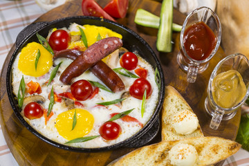 Fried eggs with cherry and sausages. Scrambled eggs with smoked sausages and cherry tomatoes in a frying pan.