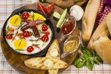 Fried eggs with cherry and sausages. Scrambled eggs with smoked sausages and cherry tomatoes in a frying pan.