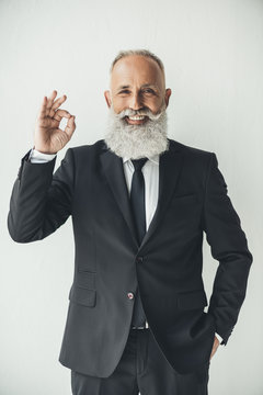 senior bearded businessman showing okay sign on light background