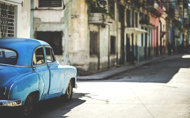 Classic 1950s car parked on street of dilapidated buildings