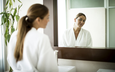 A woman standing in front of a bathroom mirror and looking at her reflection.