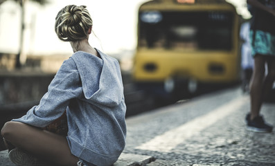 Young woman sitting on a railway station platform with a train behind.