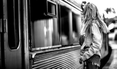 Young woman standing on a railway station platform next to a train.