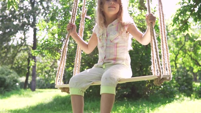 little girl swinging on a swing in summer Park. swing on ropes attached to the tree. a happy carefree childhood. slow motion