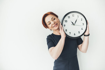 happy mature woman holding clock on white wall background