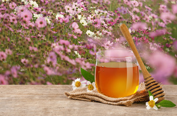 Honey Bee in glass jar with honey dipper and flowers on the wooden table, flower garden background at sunrise or sunset