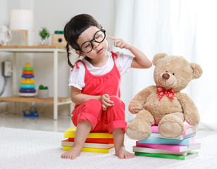 Preschooler girl learns at school. Cute child reading with teddy bear. Little girl having fun indoors at home, kindergarten or