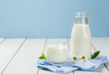 A bottle of rustic milk and glass of milk on a white wooden table on a blue background, tasty, nutritious and healthy dairy products