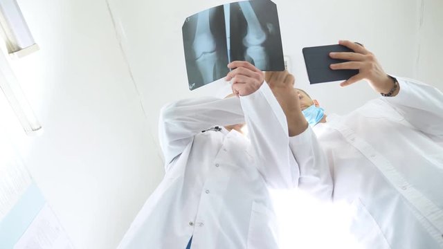 Male medics using tablet pc while consult with each other about x ray image of patient. Medical workers in hospital examine x-ray prints. Two caucasian doctors view mri picture and discussing about it