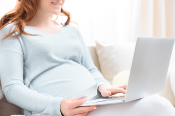 cropped view of pregnant woman with laptop and credit card shopping online at home