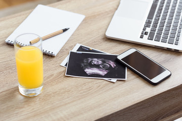 glass of juice, ultrasound scan of unborn baby and digital devices on wooden tabletop