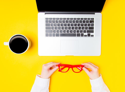 Female hands holding eyeglasses near cup of coffee and laptop