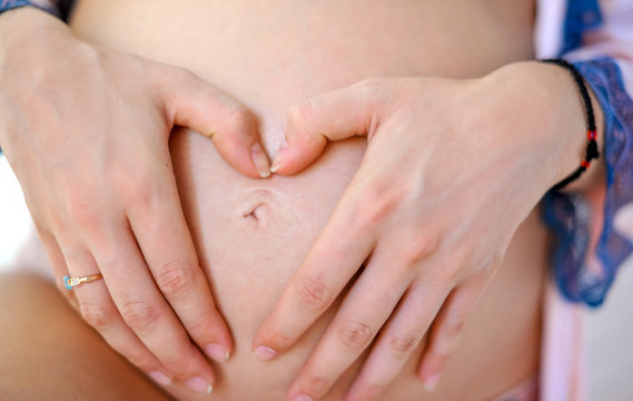 Take care of your body. The concept of a pregnancy diet. Female hands forming heart shape on belly.
