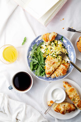 Breakfast in bed. Scrambled eggs with cheese croissants, raspberry muffin and black coffee. Morning treat concept. Composition with copy space.