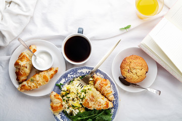 Breakfast in bed. Scrambled eggs with cheese croissants, raspberry muffin and black coffee. Morning treat concept. Composition with copy space.