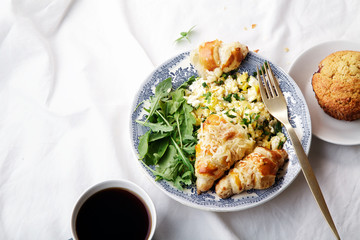 Breakfast in bed. Scrambled eggs with cheese croissants, raspberry muffin and black coffee. Morning treat concept. Composition with copy space.