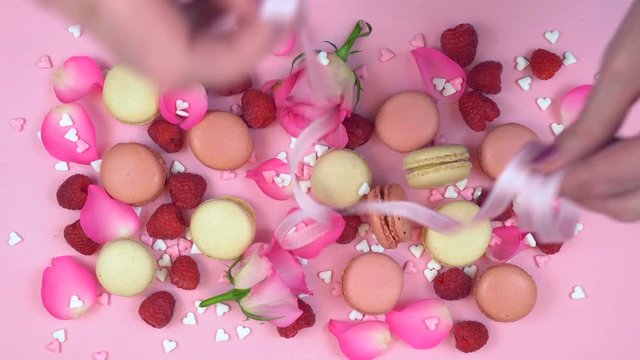 Petit Fours presentation of macarons with berries and rose petals on pink wood overhead real time final touches.