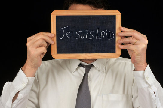 Homme tenant un e ardoise cachant son visage sur laquelle est &eacute;crit je suis laid 