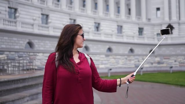Young girl takes a photo near a beautiful building on a selfie stick. HD, 1920x1080. Slow motion