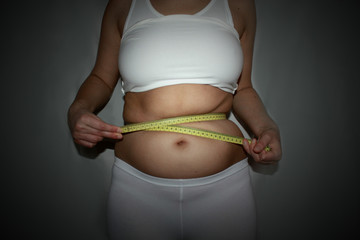 Woman measuring waistline with centimeter tape. Dark vignette background. Horizontal photo of a...