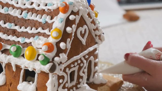 Female decorates a gingerbread house with a cream inside the piping bag